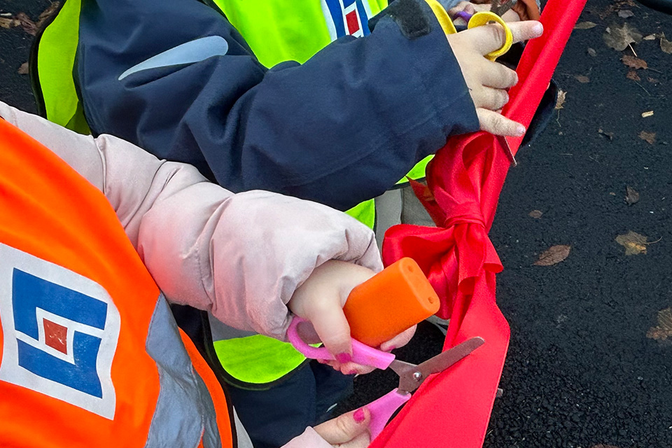 Två barnhänder klipper av ett rött sidenband med saxar