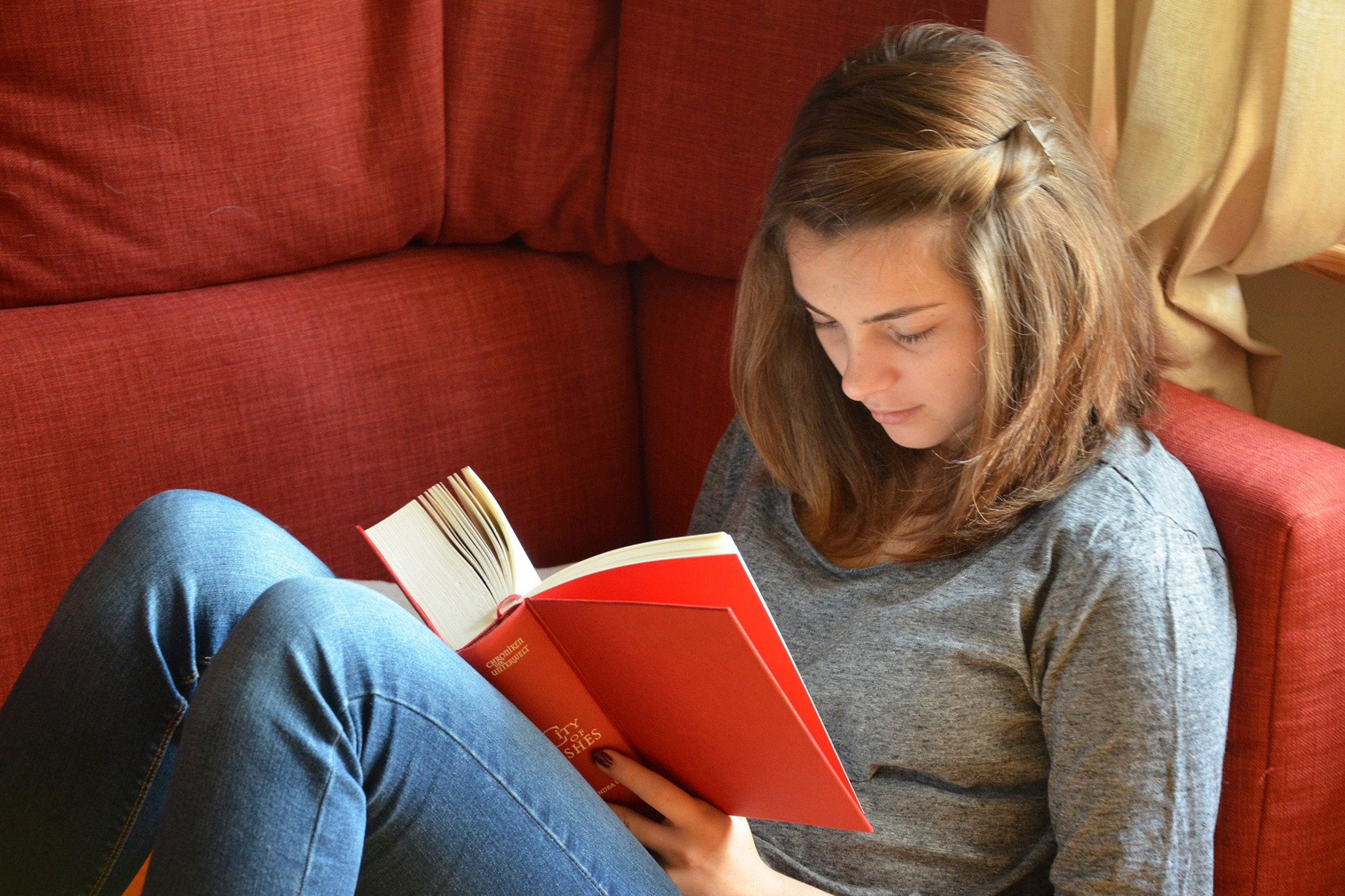 Ung kvinna sitter i röd soffa och läser en bok