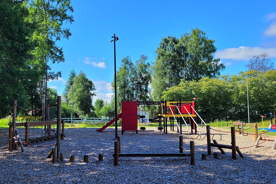 Bild från lekplats och balanshinder i trä. I bakgrunden syns en stor klätterställning med en rutchelkana.