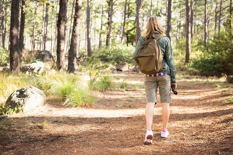 En kvinna i med ryggsäck på ryggen promenerar på en skogsväg