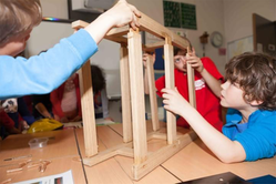 Tre personer bygger en konstruktion i trä på ett bord