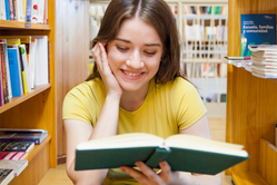 Flicka i gul tröja sitter mellan bibliotekshyllor på golvet och läser.