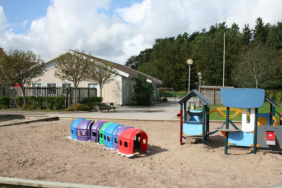 Stor sandlåda där en lång tunnel är byggd av olikfärgade små plasthus. I bakgrunden syns en beige träbyggnad