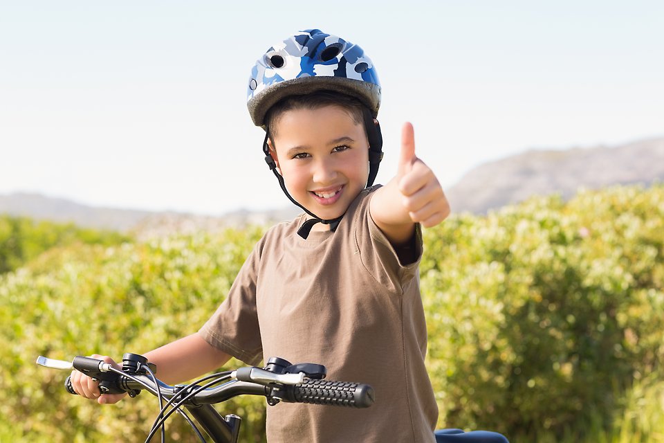 En pojke med blå hjälm på huvudet har stannat med sin cykel och gör tummen upp mot kameran